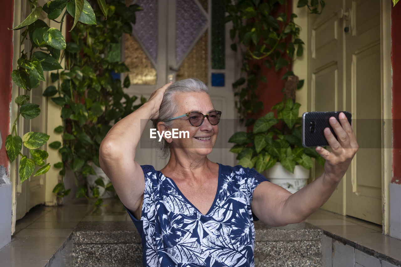 Cheerful senior woman taking selfie on steps at home