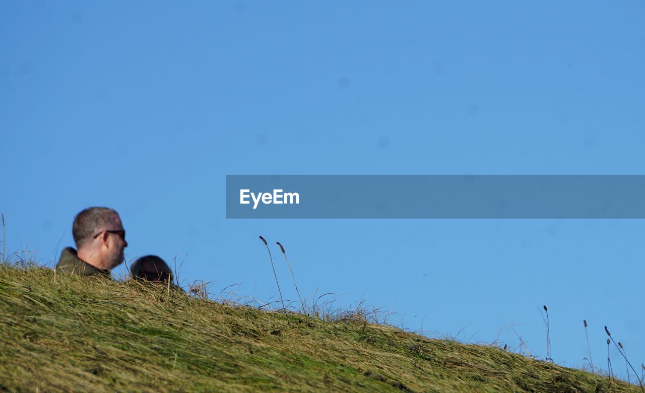 sky, grass, nature, copy space, blue, plant, one person, clear sky, men, hill, adult, land, day, grassland, person, animal themes, leisure activity, animal, outdoors, landscape, field, relaxation, sitting, mammal, looking, environment, meadow, animal wildlife, lifestyles, portrait