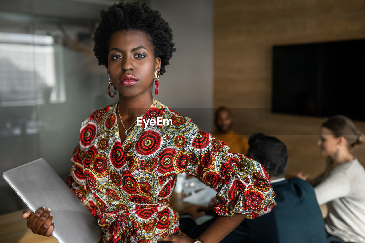 Portrait of beautiful woman holding laptop while standing at office