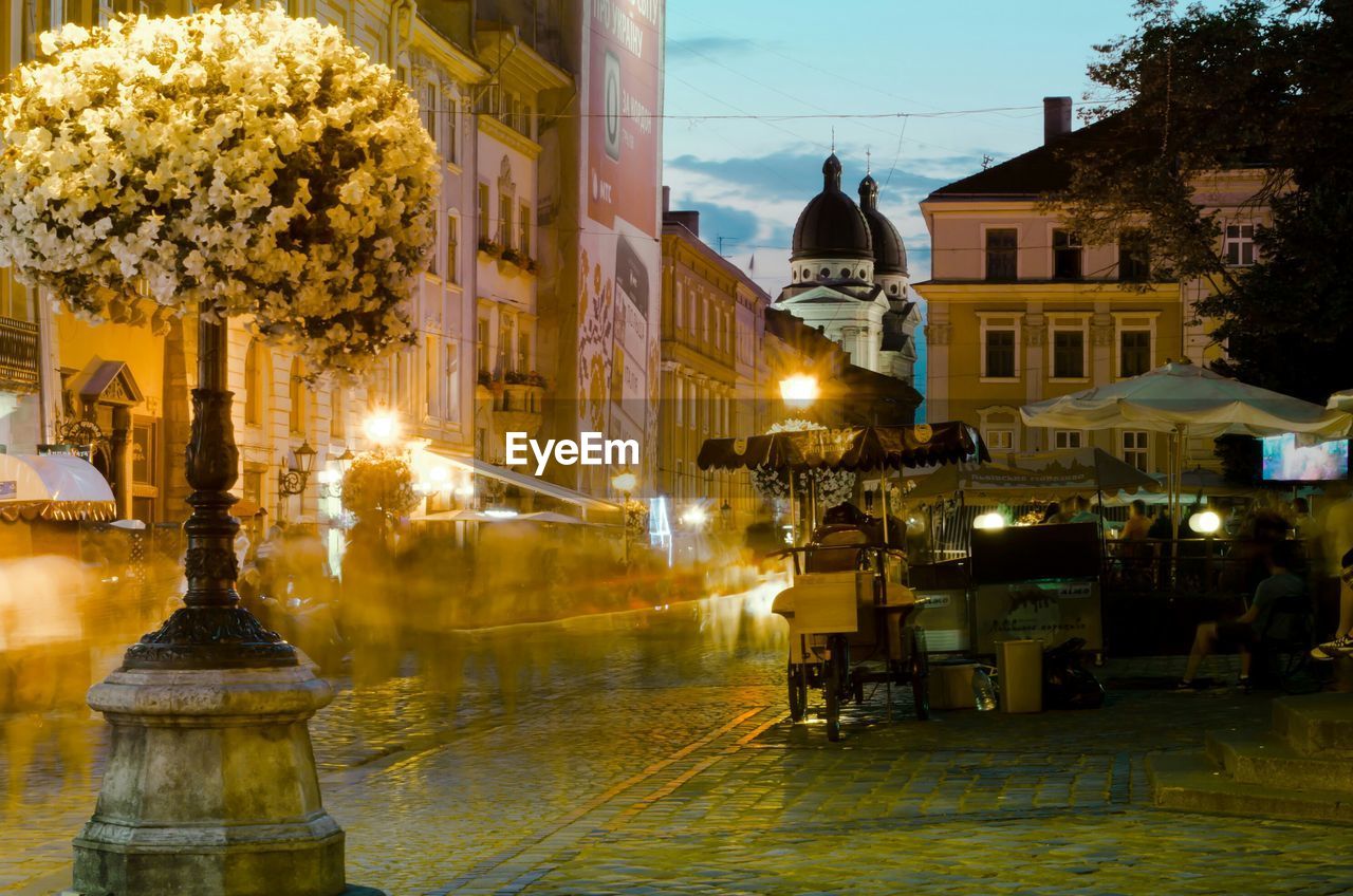 Illuminated buildings by wet street at night.