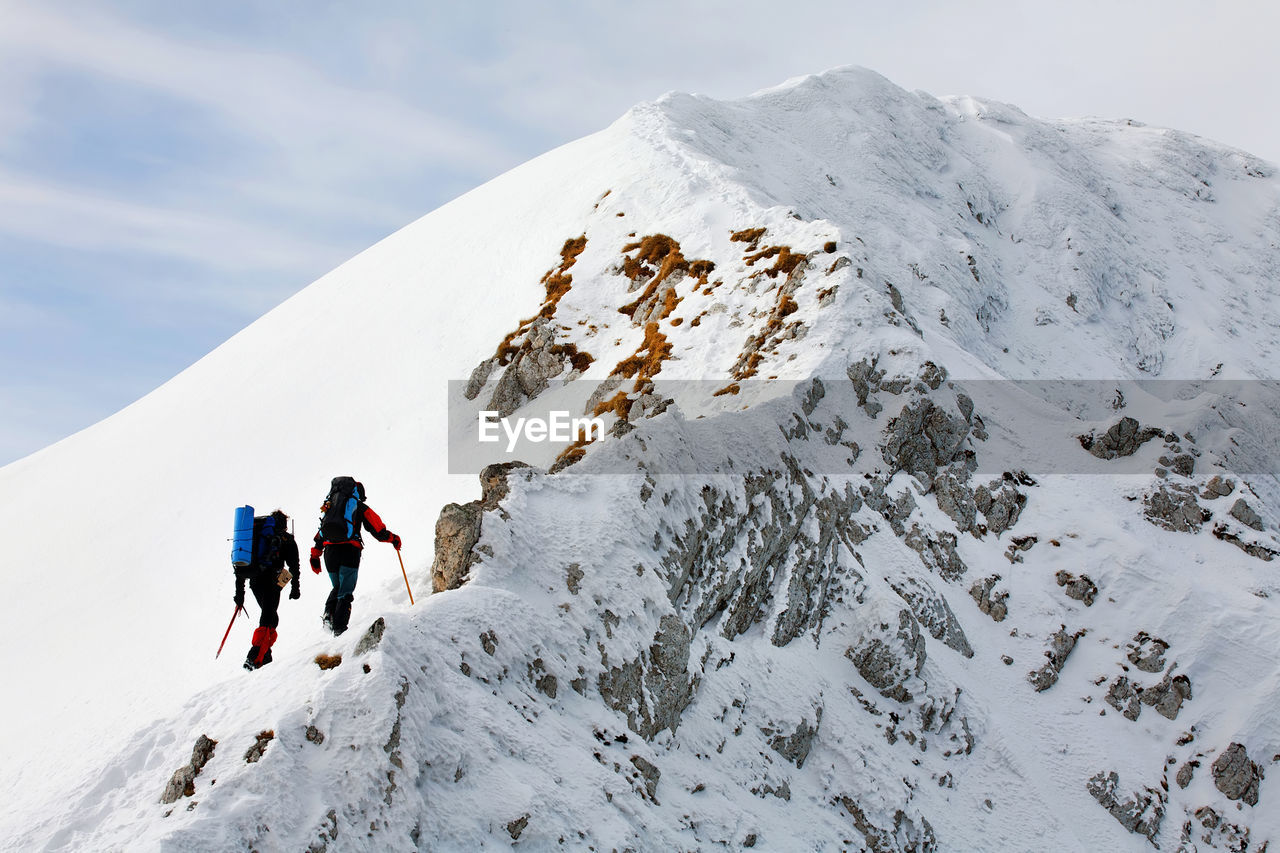 Low angle view of mountaineers climbing snowcapped mountain against sky