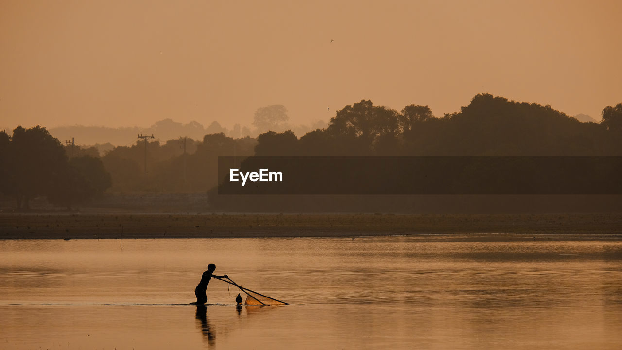 Silhouette of man in lake during sunset