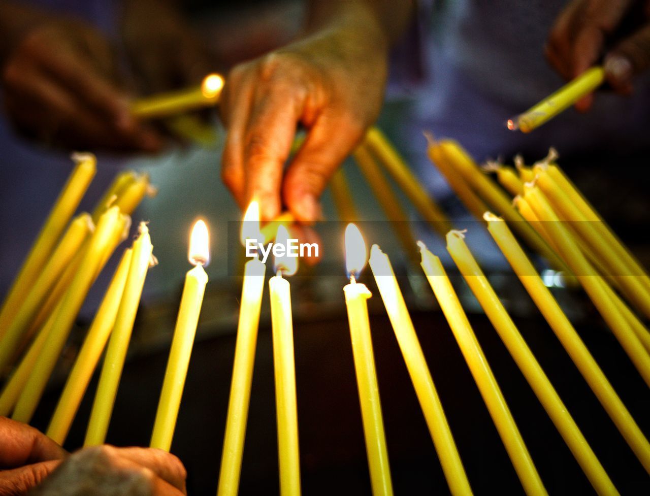 CLOSE-UP OF HAND HOLDING YELLOW BURNING CANDLES