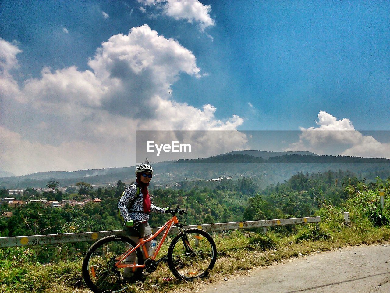 Woman with bicycle on roadside against cloudy sky