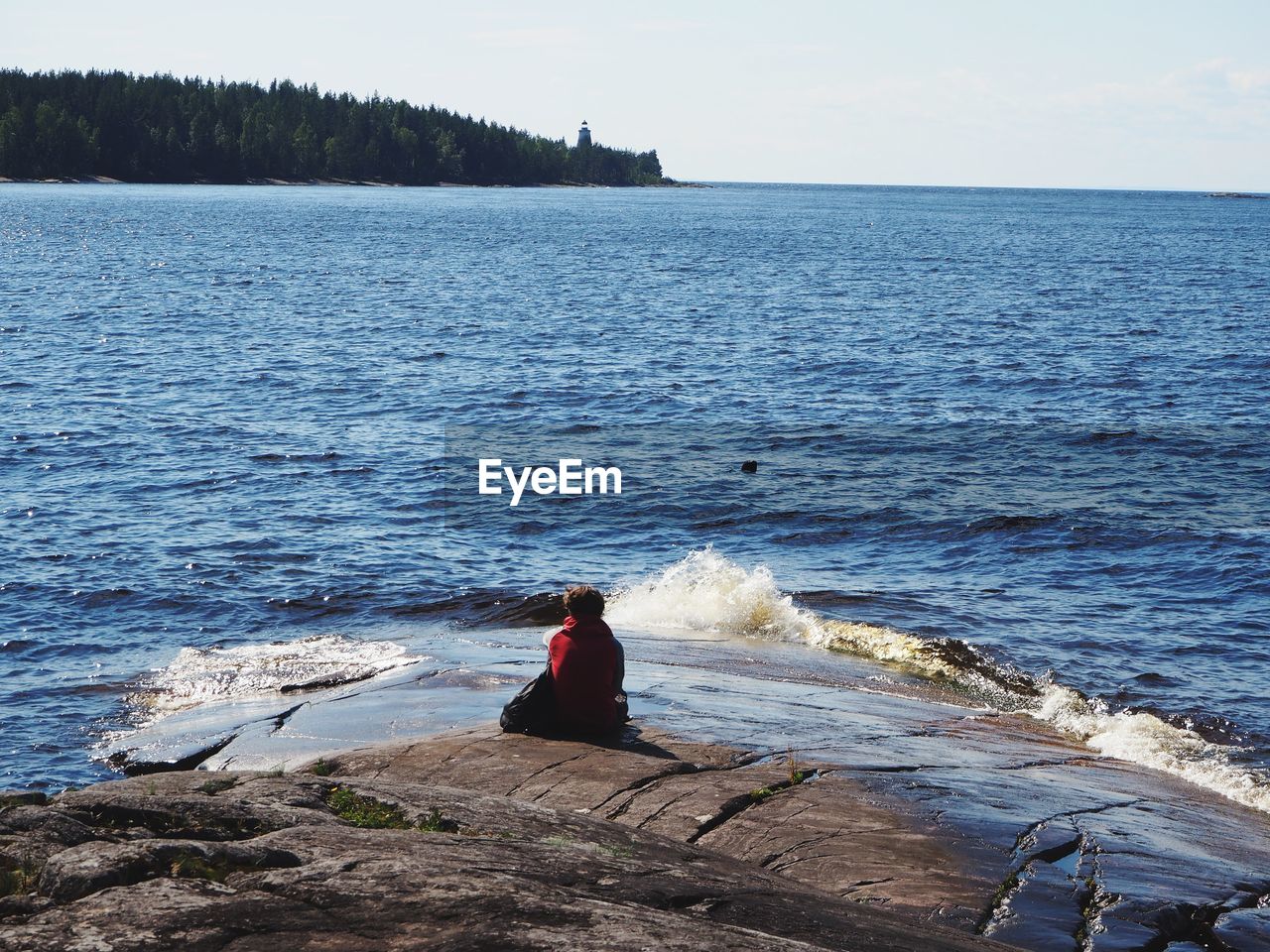 Rear view of man sitting on rock by sea against sky