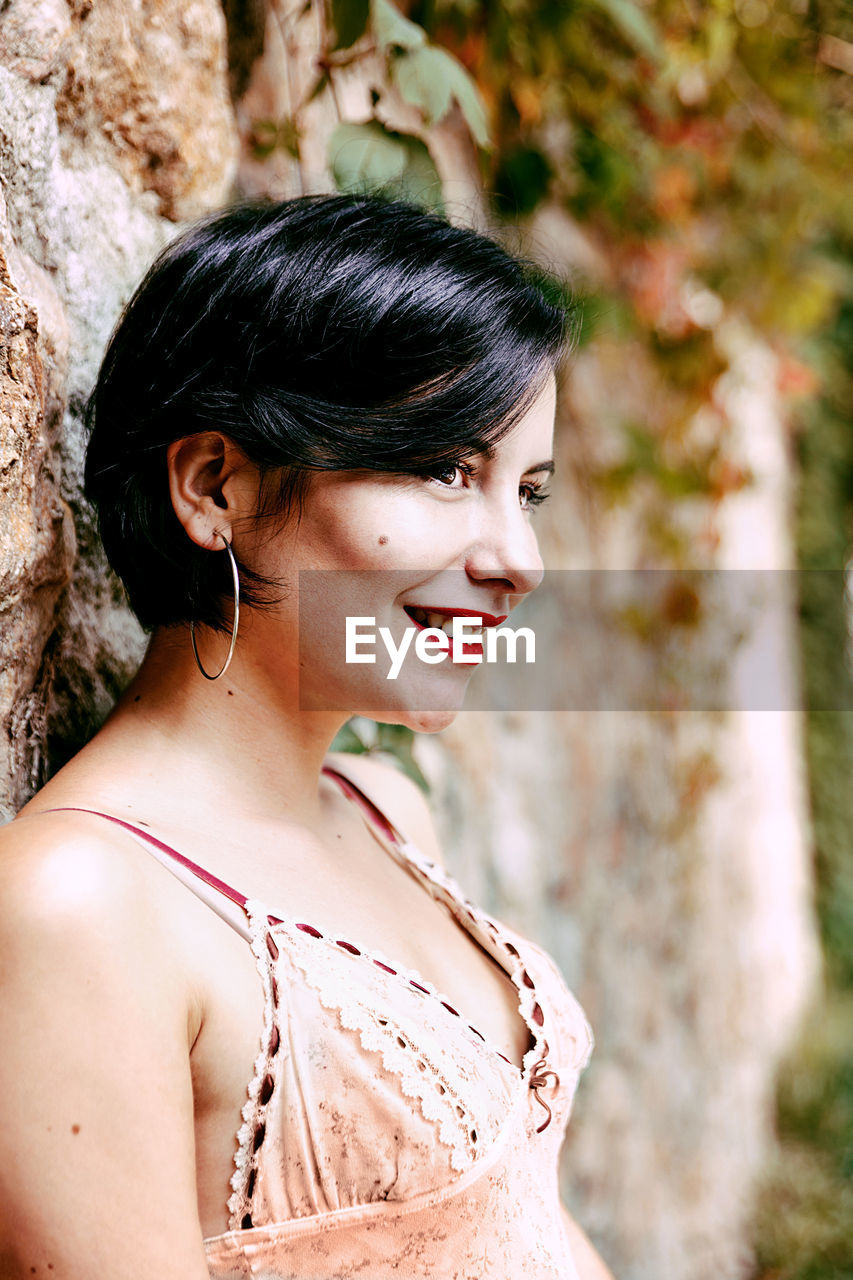 Smiling young woman standing by wall standing outdoors