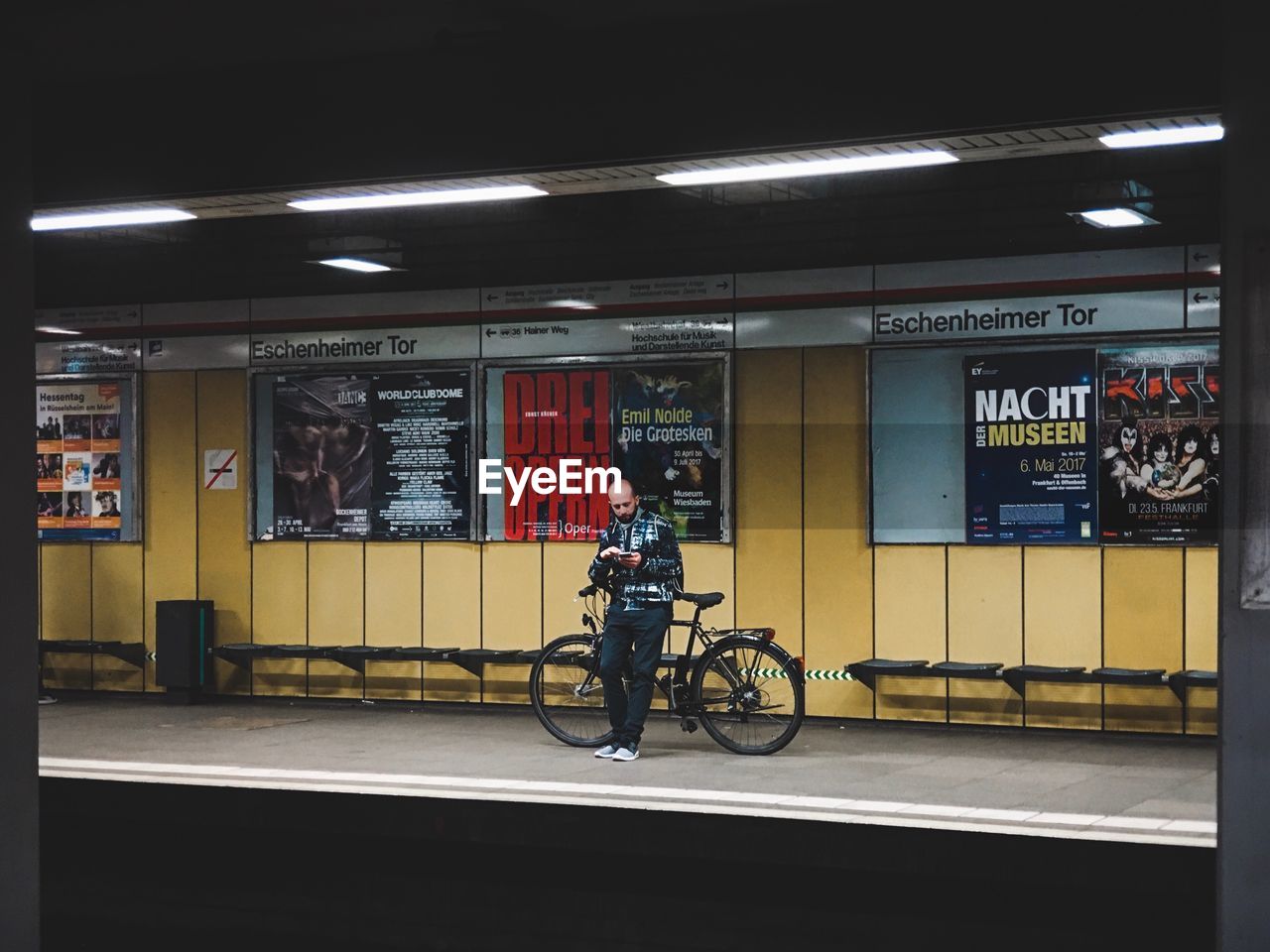 MAN WITH BICYCLE STANDING BY ILLUMINATED STORE