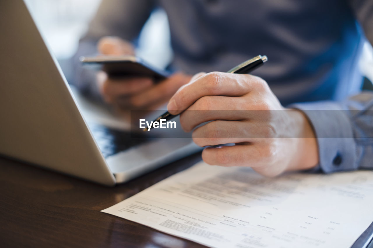 Man at desk using cell phone and holding ball pen in his hand, close-up