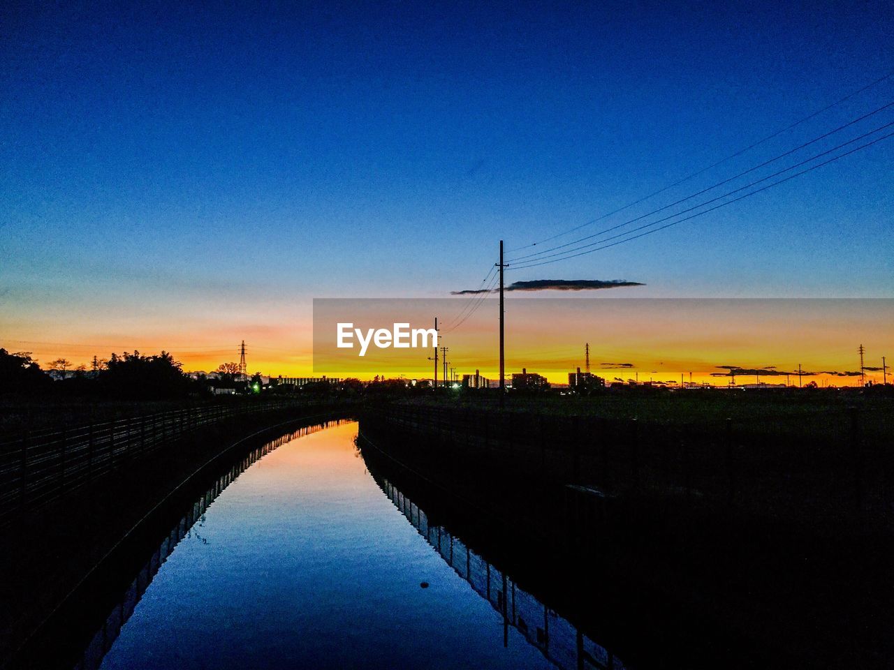 Canal amidst silhouette field against sky at dusk