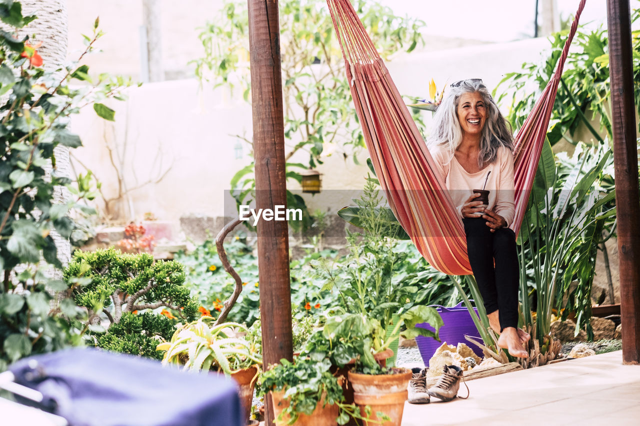 Smiling woman sitting on hammock by plants