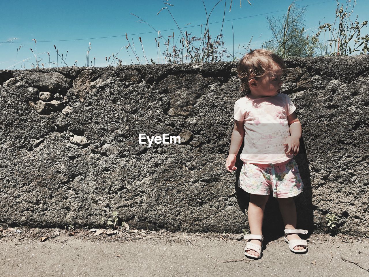 Full length of child standing against concrete wall during sunny day