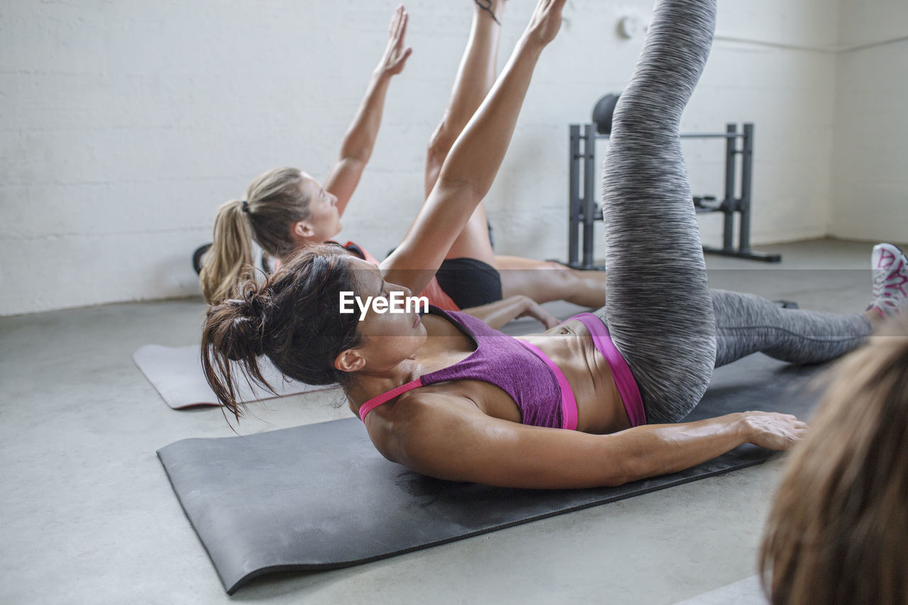 Female athletes stretching body while lying on exercise mats in gym