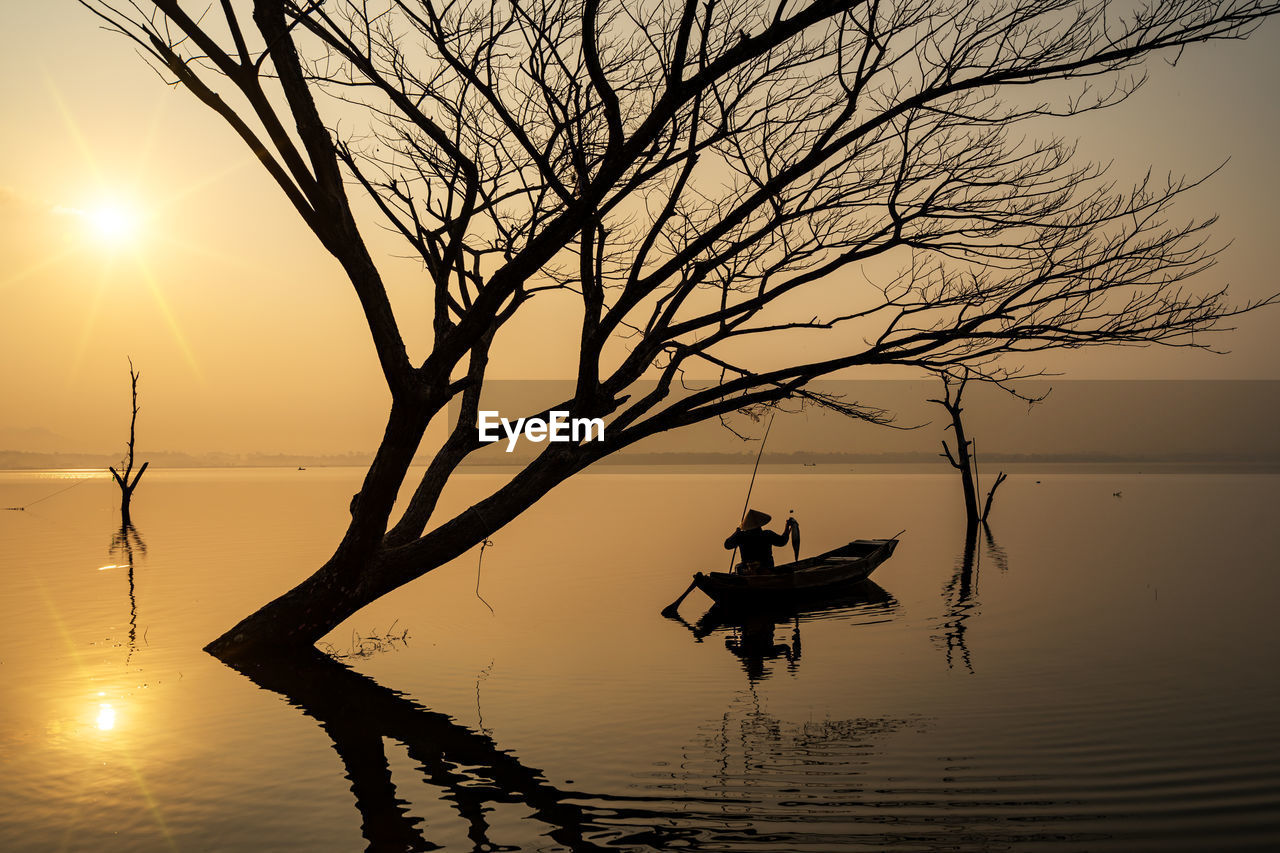 Man sitting in boat on sea against sky during sunset