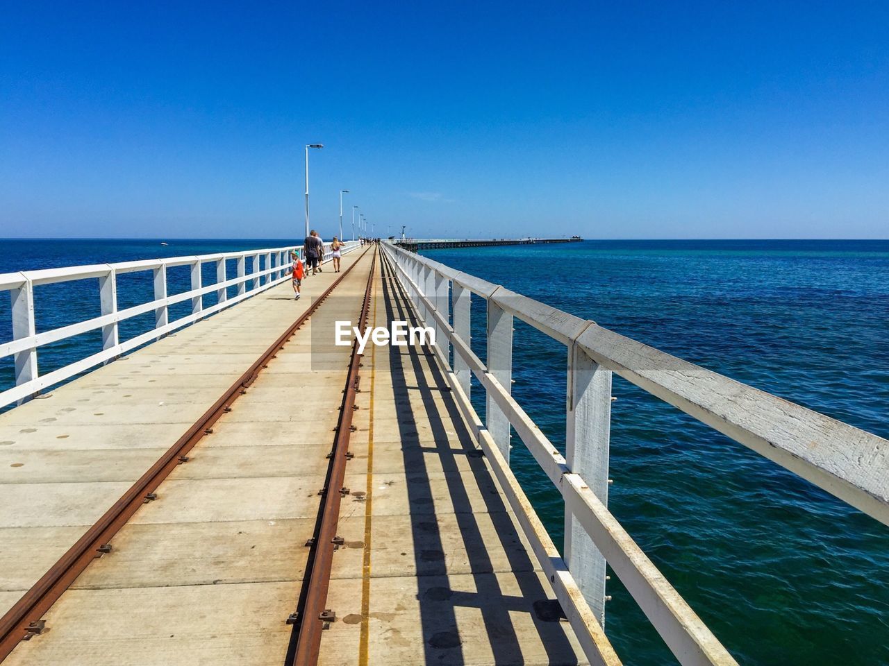 Pier on sea against clear blue sky