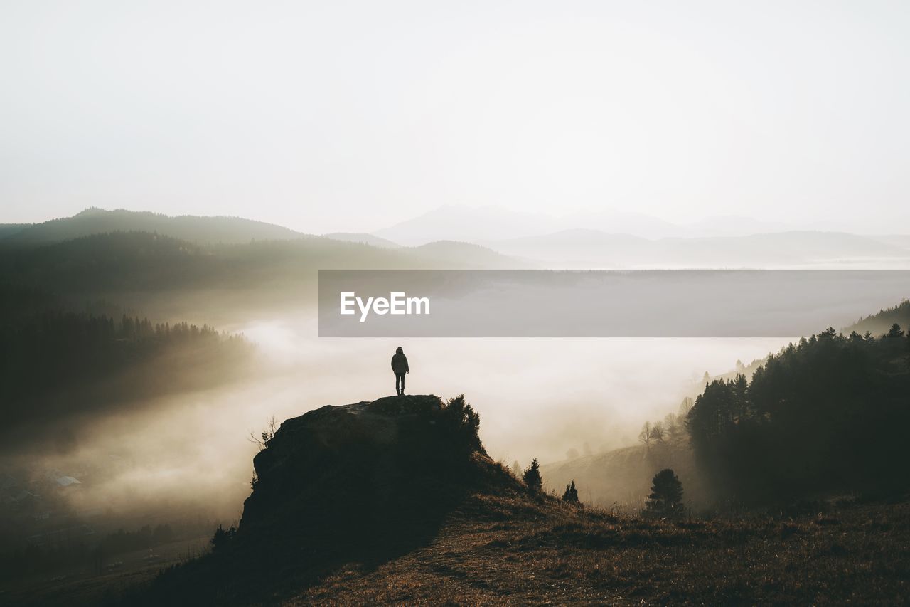 rear view of woman standing on mountain against sky during sunset