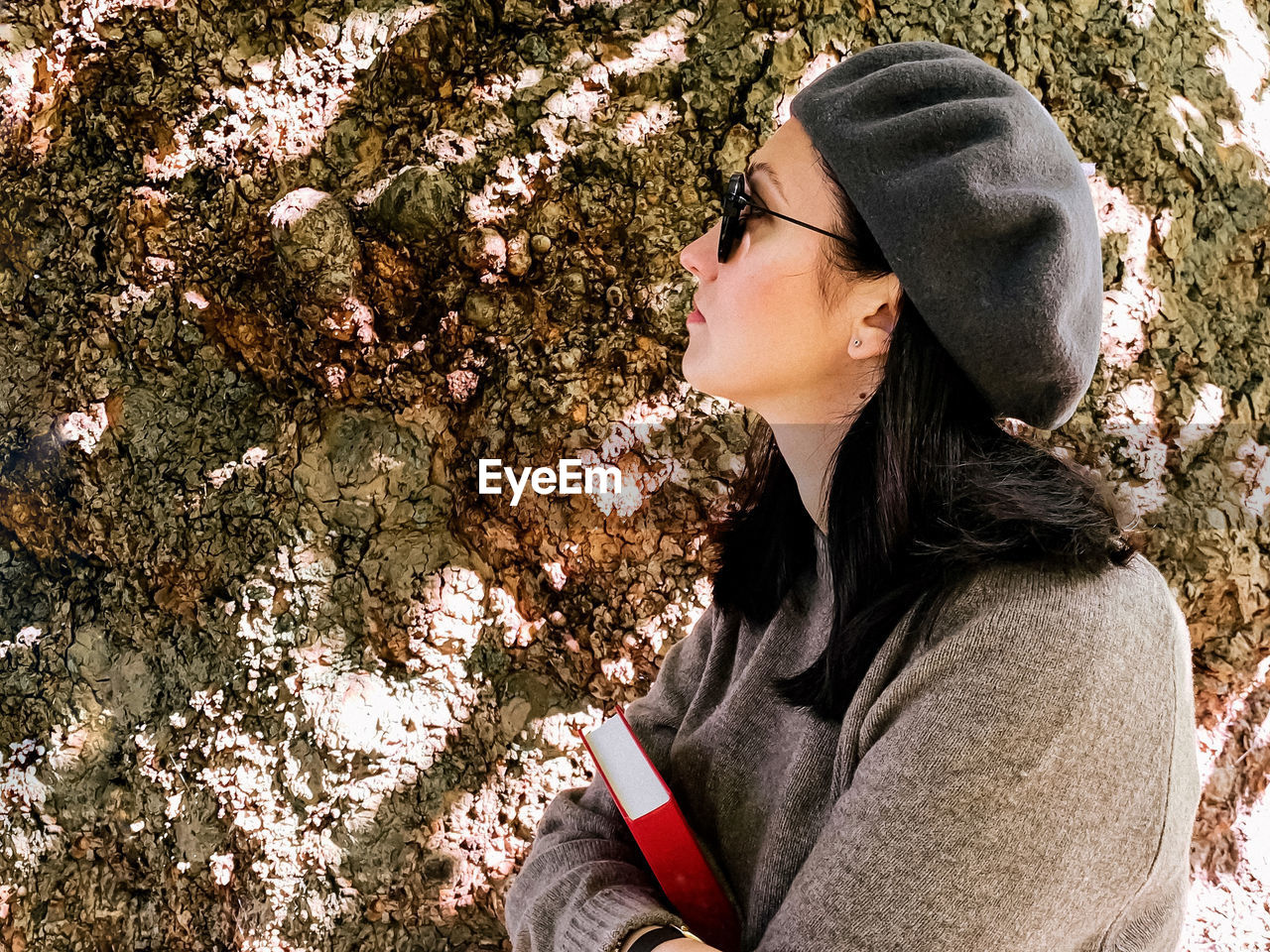 Young candid woman in casual clothes  french beret by old tree. holding book. confident young adult