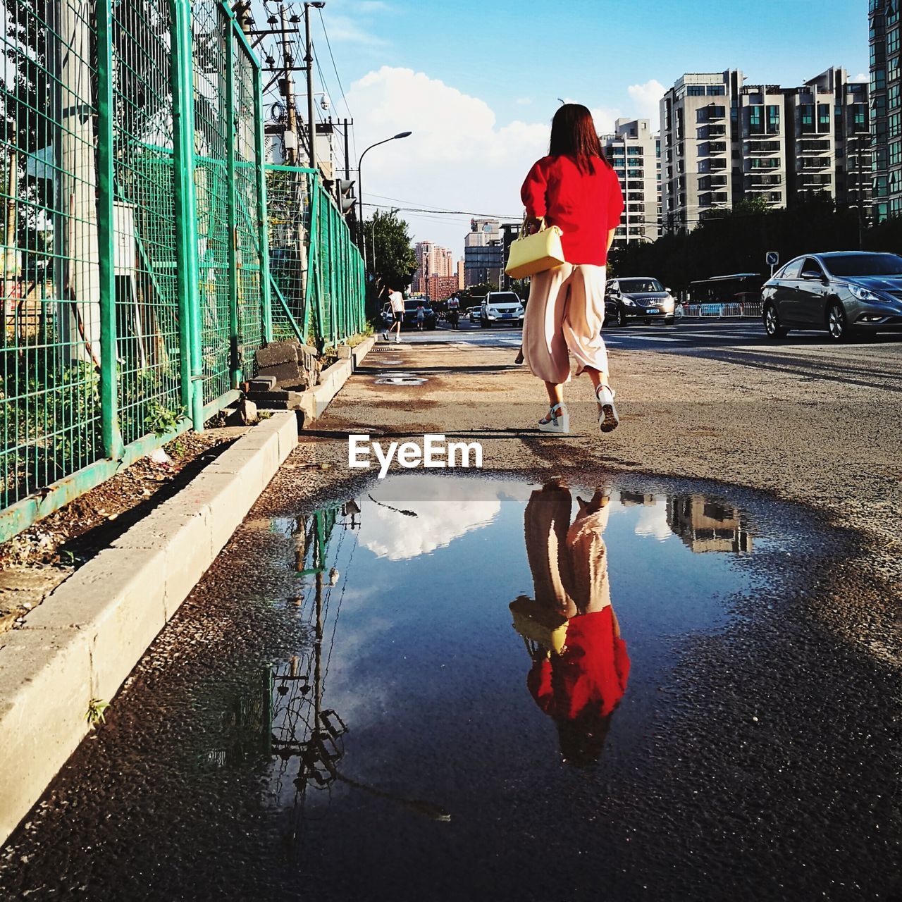 Reflection of woman walking on puddle in city