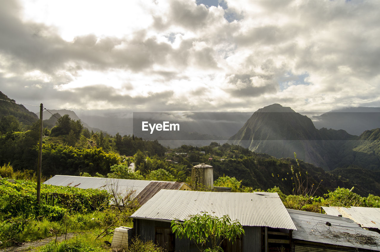 Houses by mountains against cloudy sky