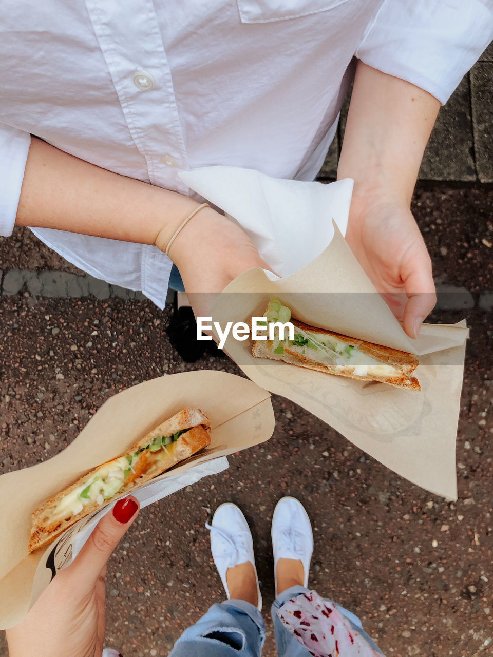 Enjoying grilled cheese at a food stand. pov shot of two girls holding sandwiches. 