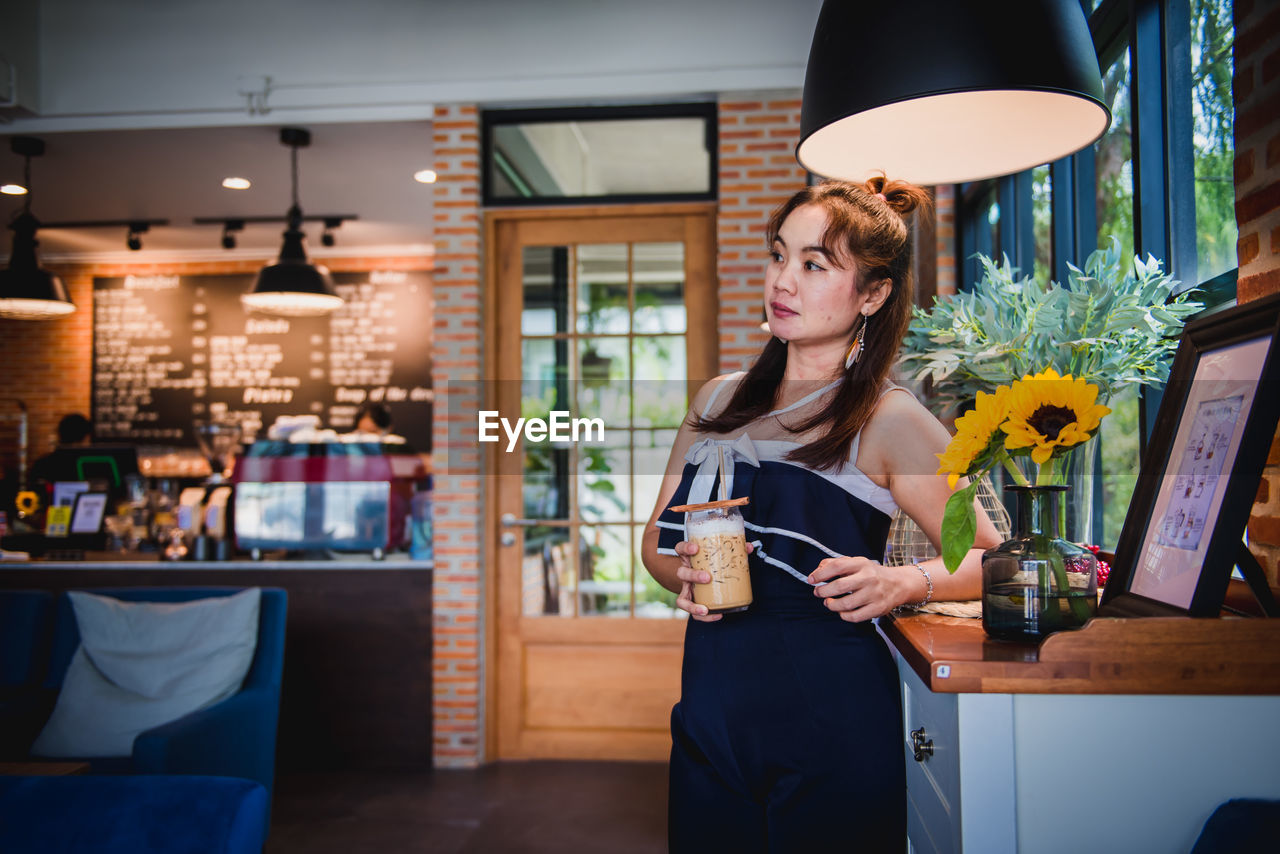 Woman holding coffee while standing by table in cafe