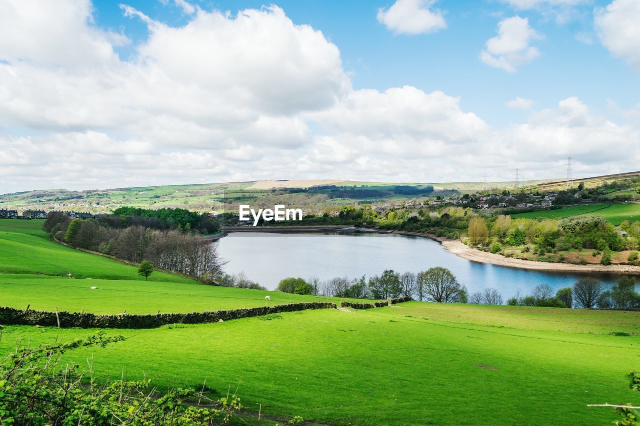 Scenic view of grassy field by lake against sky