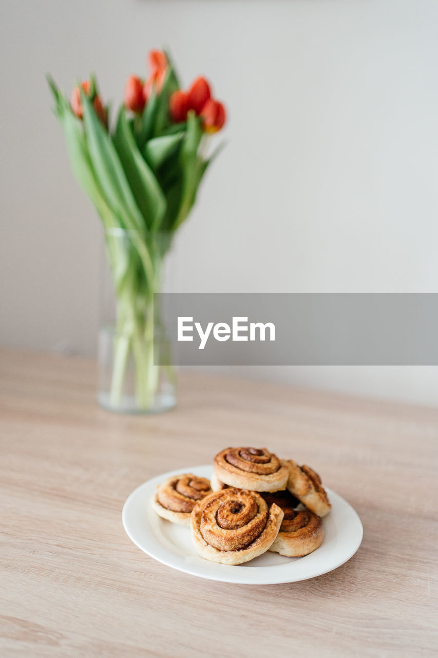 Home baked cinnamon buns on a plate in front of tulips