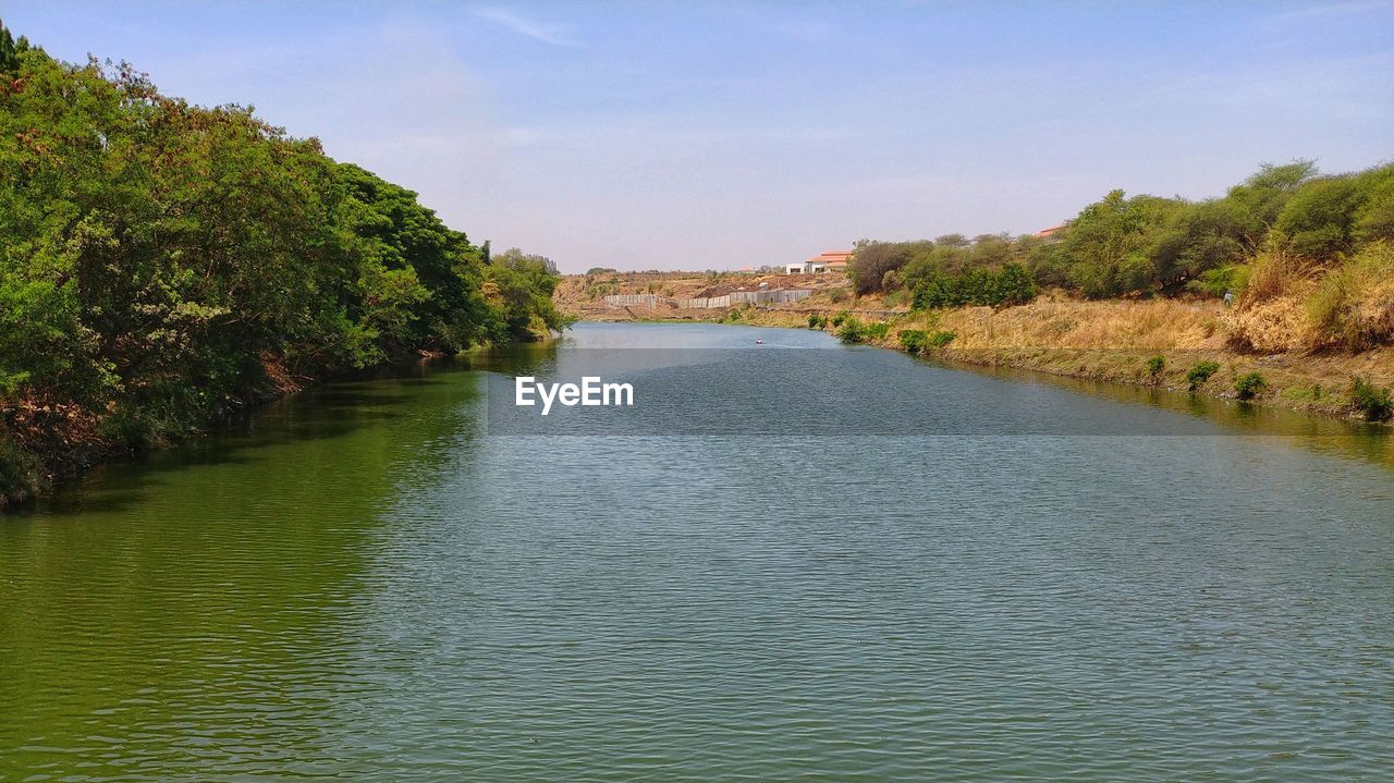 RIVER FLOWING AMIDST TREES AGAINST SKY