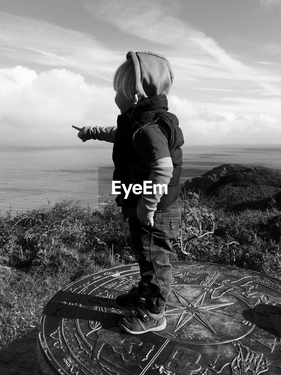 Side view of boy standing on metallic structure against sky