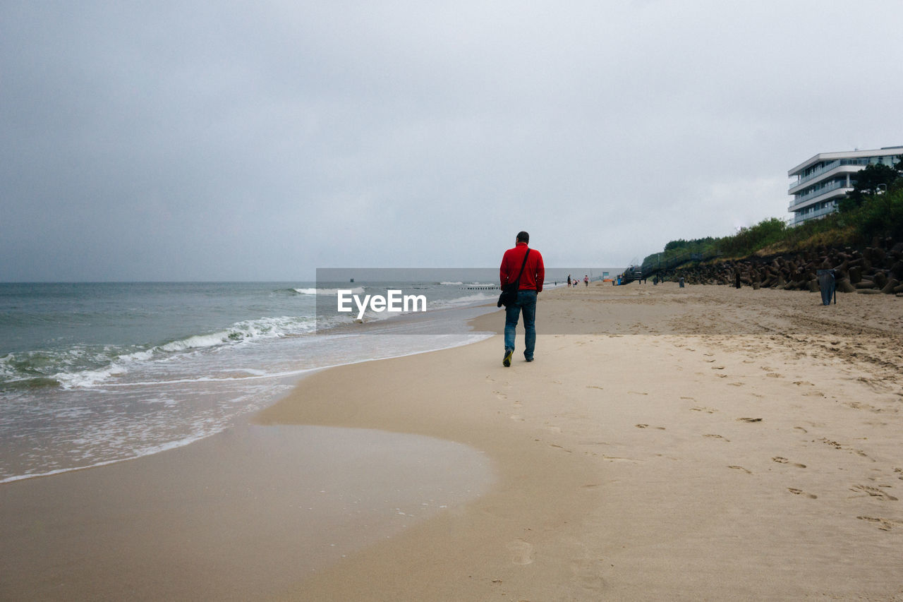Mielno, poland, baltic sea - middle aged man walking on ocean beach sand on cloudy and rainy day