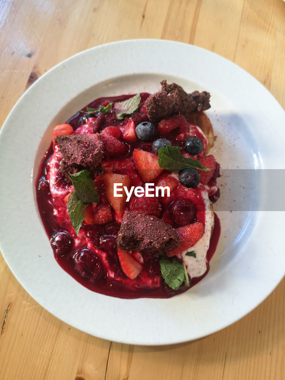High angle view of forest fruits in sauce with brownie bits in plate on table