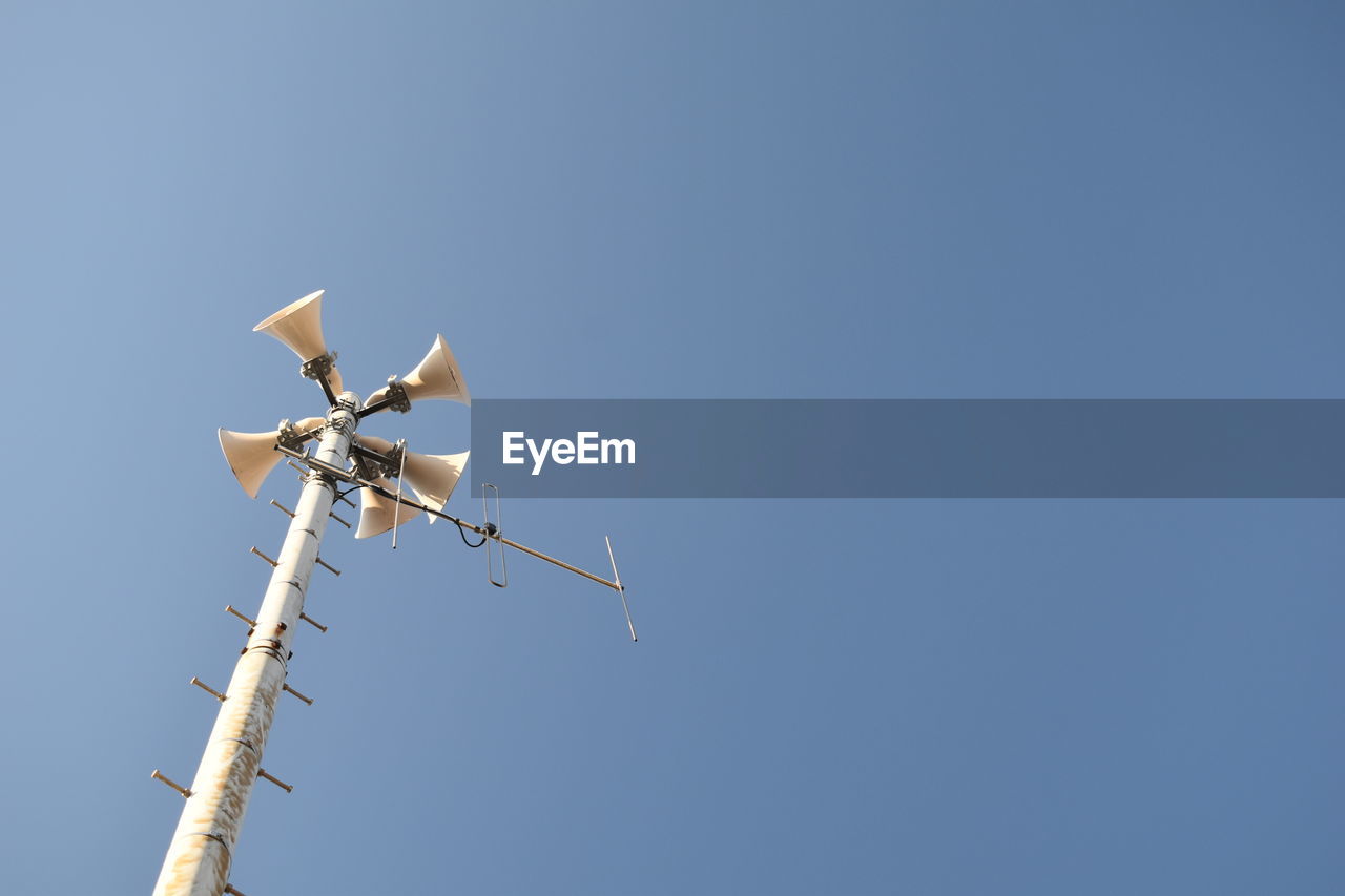 Low angle view of loud speakers against clear blue sky