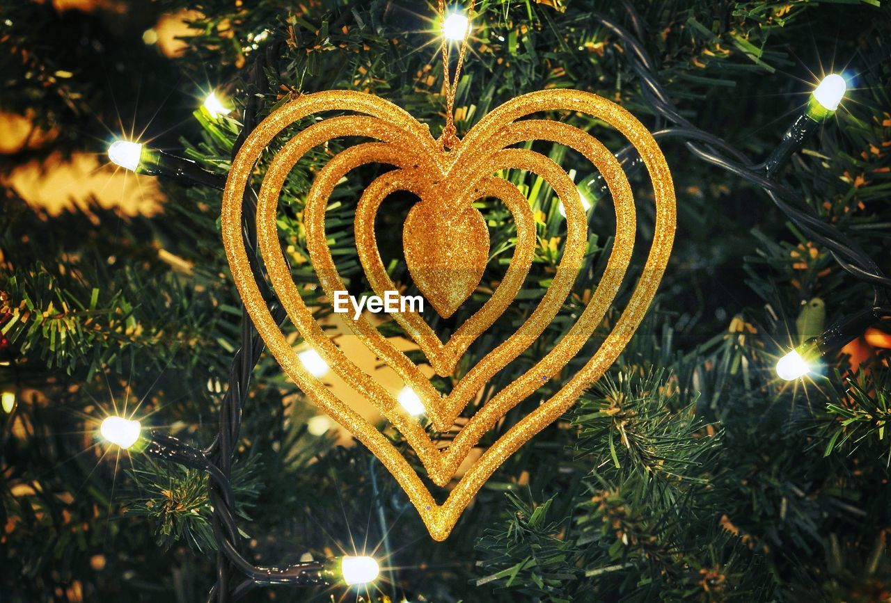 Close-up of golden heart shape hanging on illuminated christmas tree