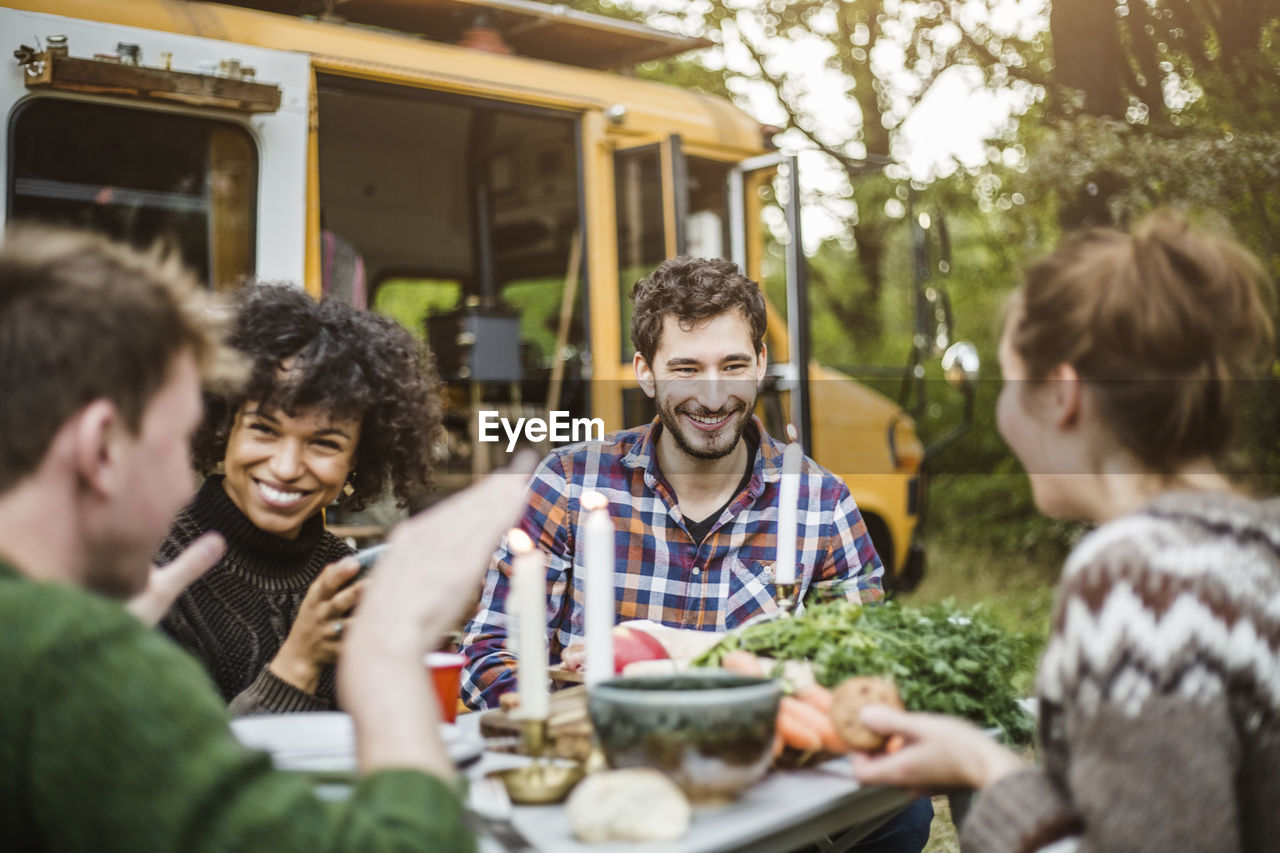 Happy friends enjoying while talking at table during camping