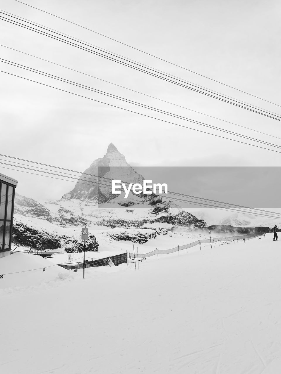 snow, cold temperature, winter, environment, cable, landscape, sky, nature, mountain, scenics - nature, electricity, beauty in nature, land, power line, day, travel destinations, travel, architecture, snowcapped mountain, no people, black and white, tranquil scene, tranquility, monochrome, outdoors, cloud, mountain range, non-urban scene, built structure, frozen, white, electricity pylon, transportation, tourism, monochrome photography