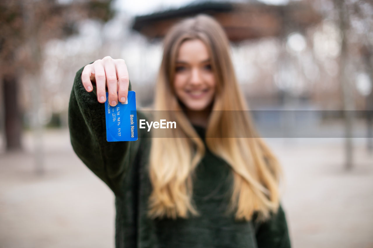 Portrait of woman holding credit card while standing in park