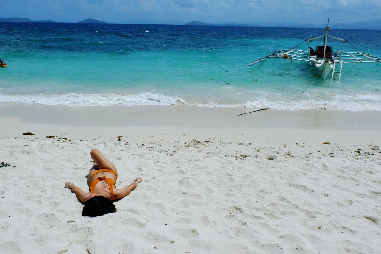 Woman sunbathing on sand at beach against sky