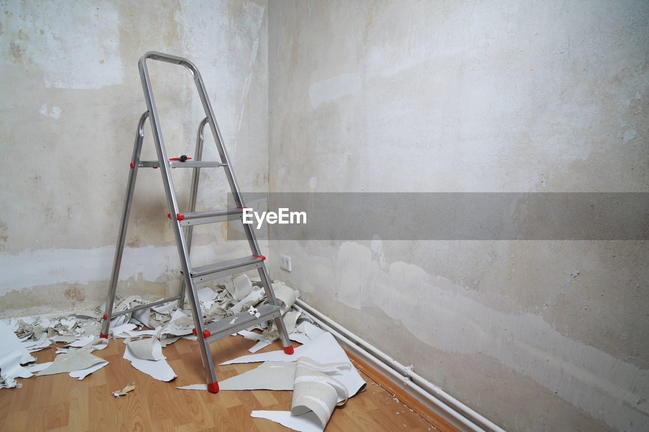 Ladder in corner of peeled wall at home