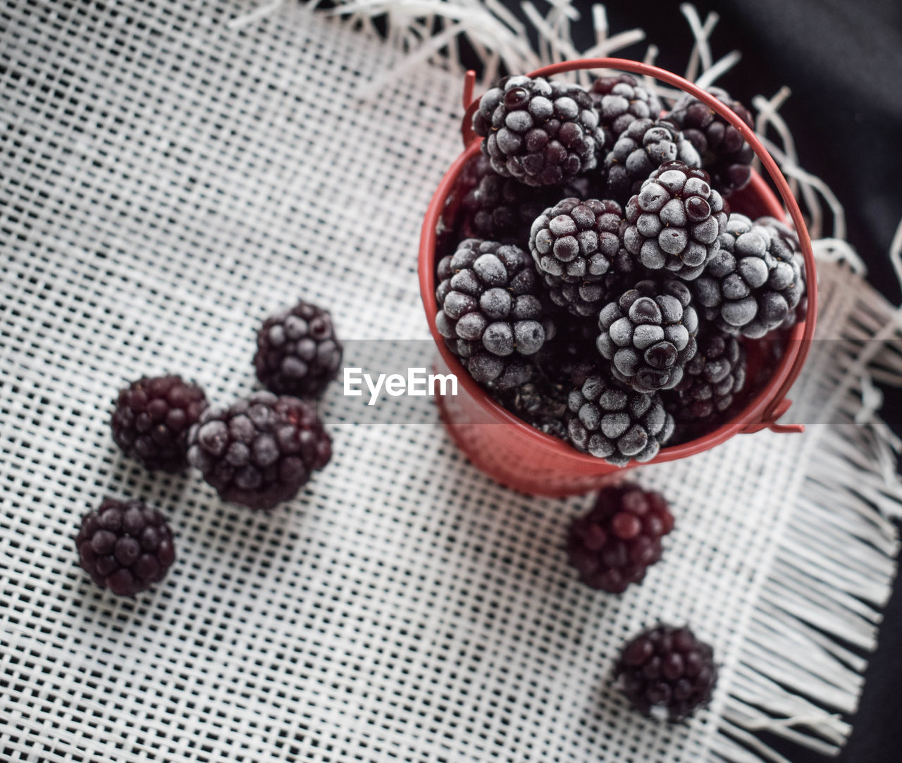 Frozen blueberries in a red bucket on the table in summer 2018