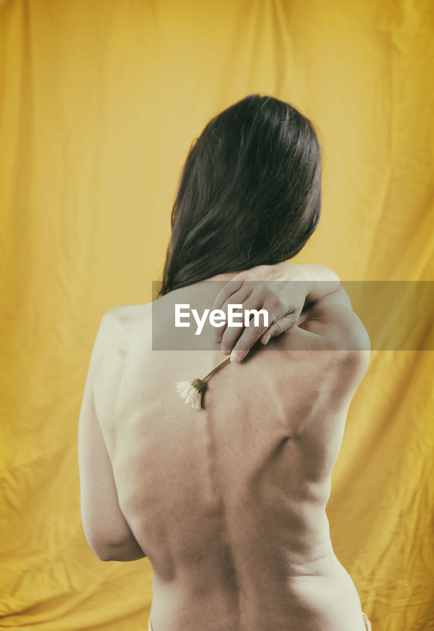 Woman in yellow satin dress showing her back in a romantic attitude with a daisy