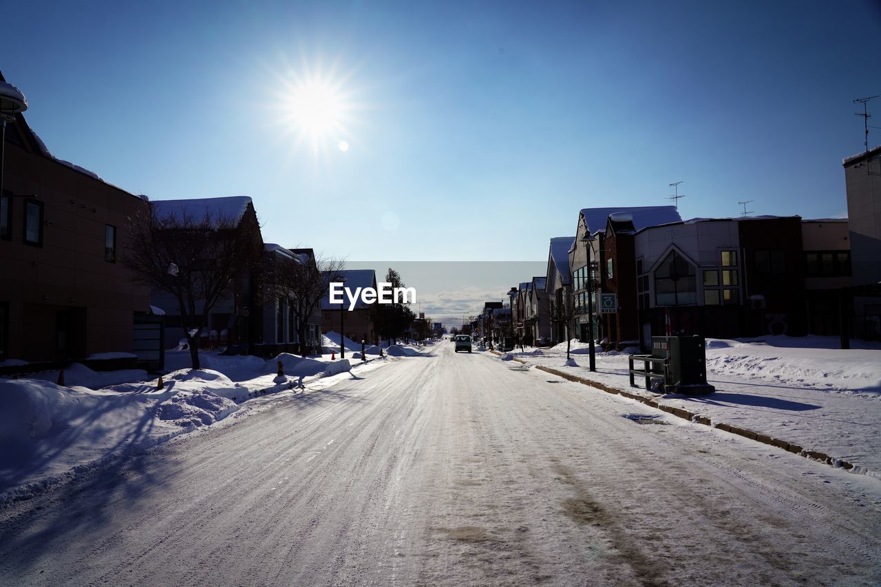 Road amidst snow covered buildings against sky