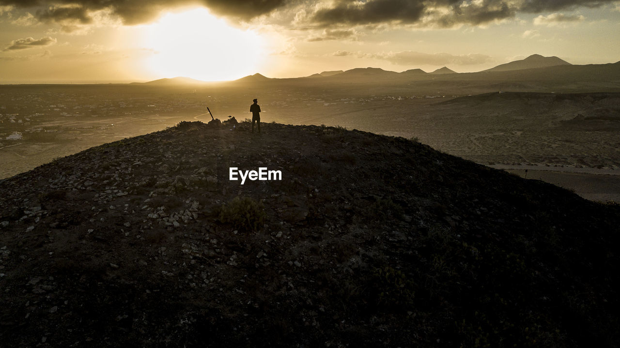 Silhouette person standing on rock against sky during sunset