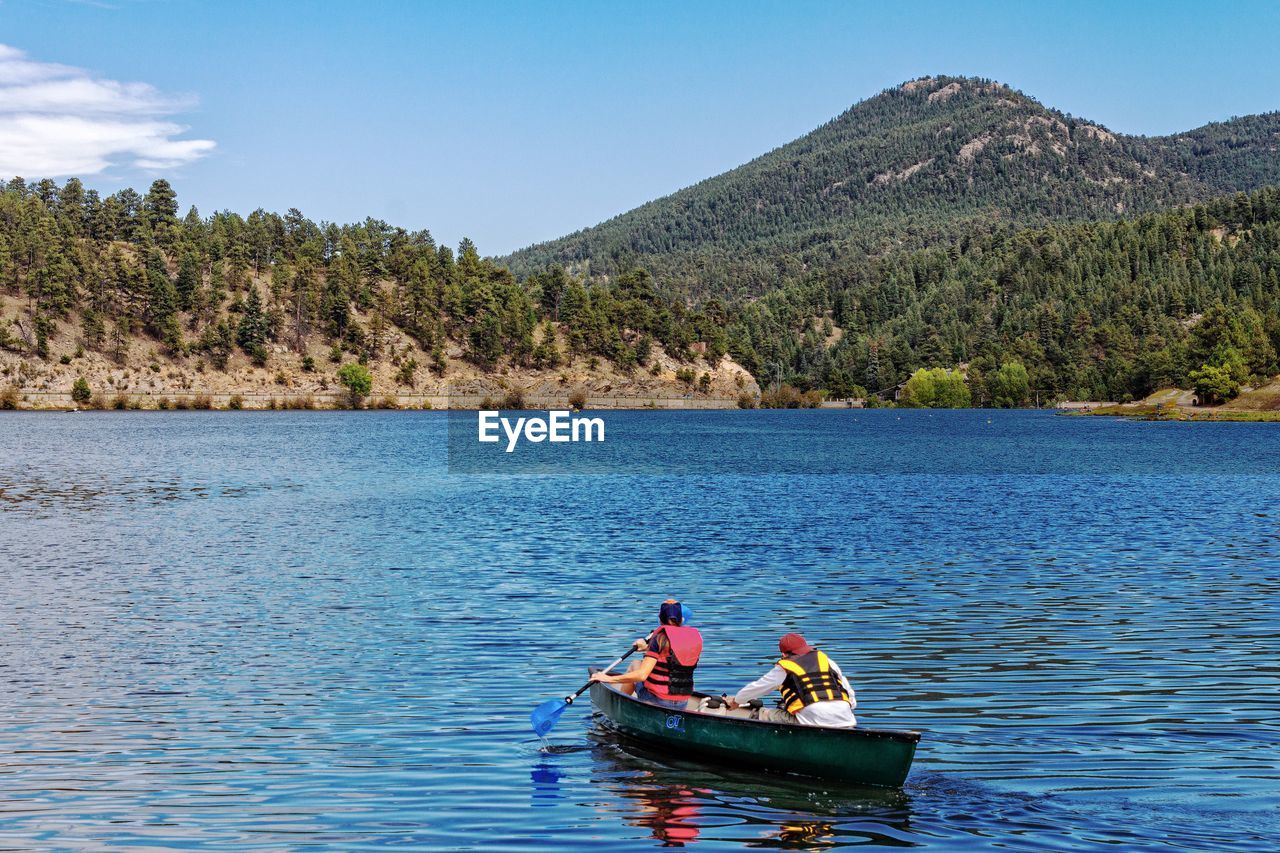 PEOPLE IN BOAT ON SEA AGAINST MOUNTAIN