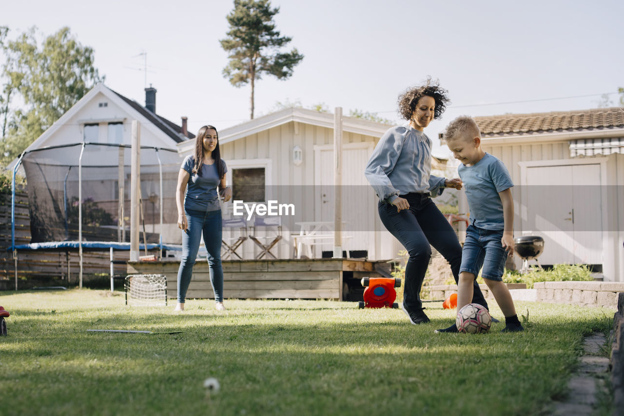 Mother and son playing soccer while woman standing in backyard