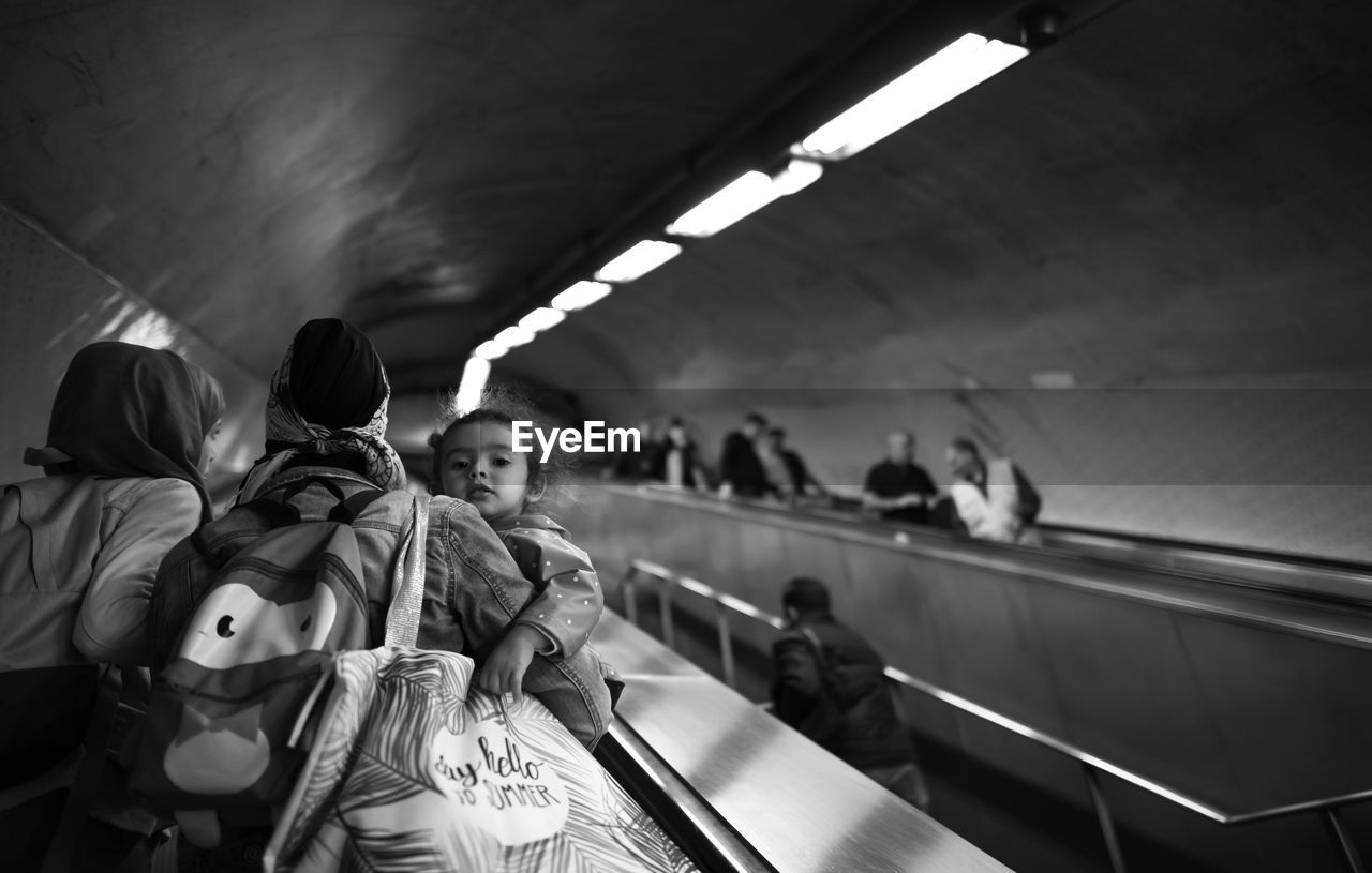 REAR VIEW OF PEOPLE STANDING BY ESCALATOR