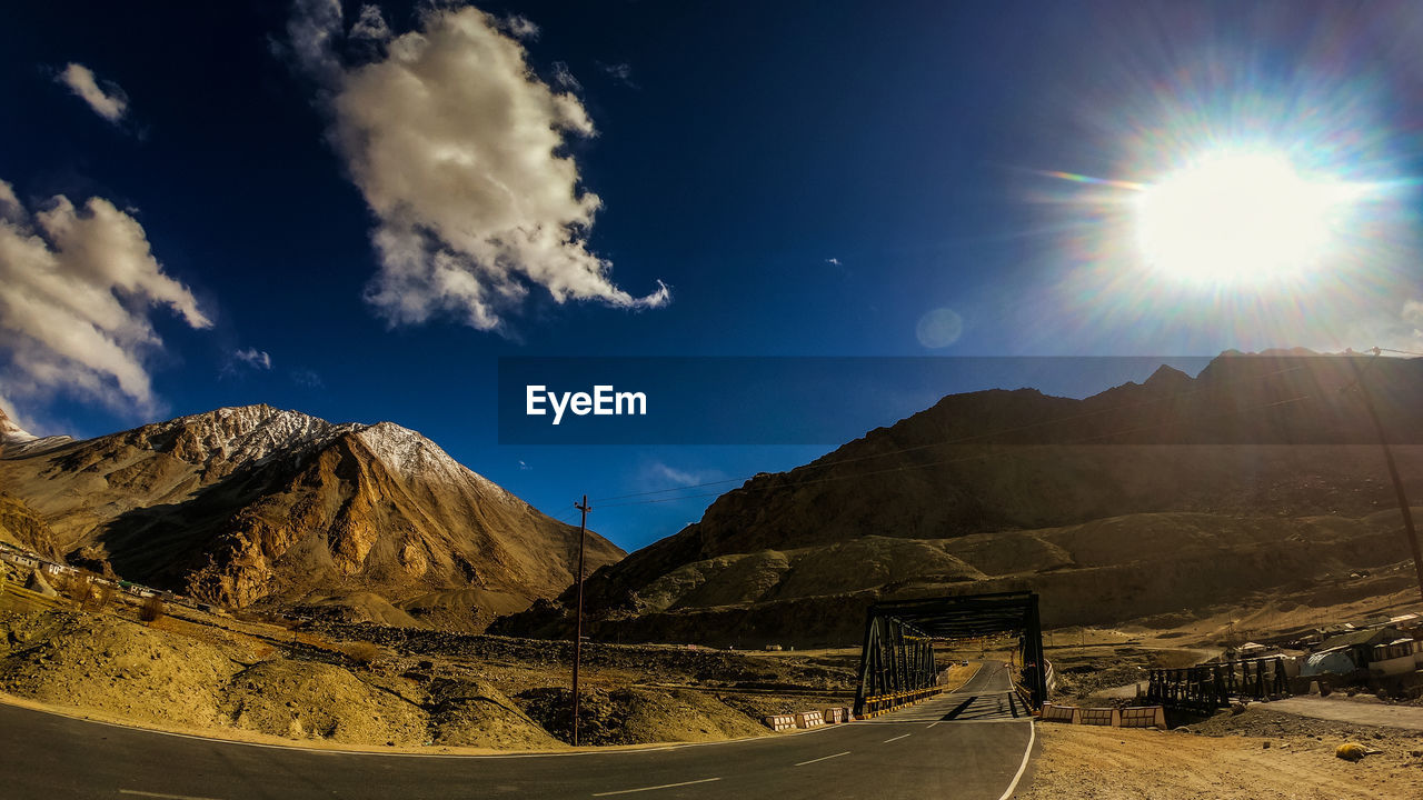 ROAD BY MOUNTAINS AGAINST BRIGHT SUN