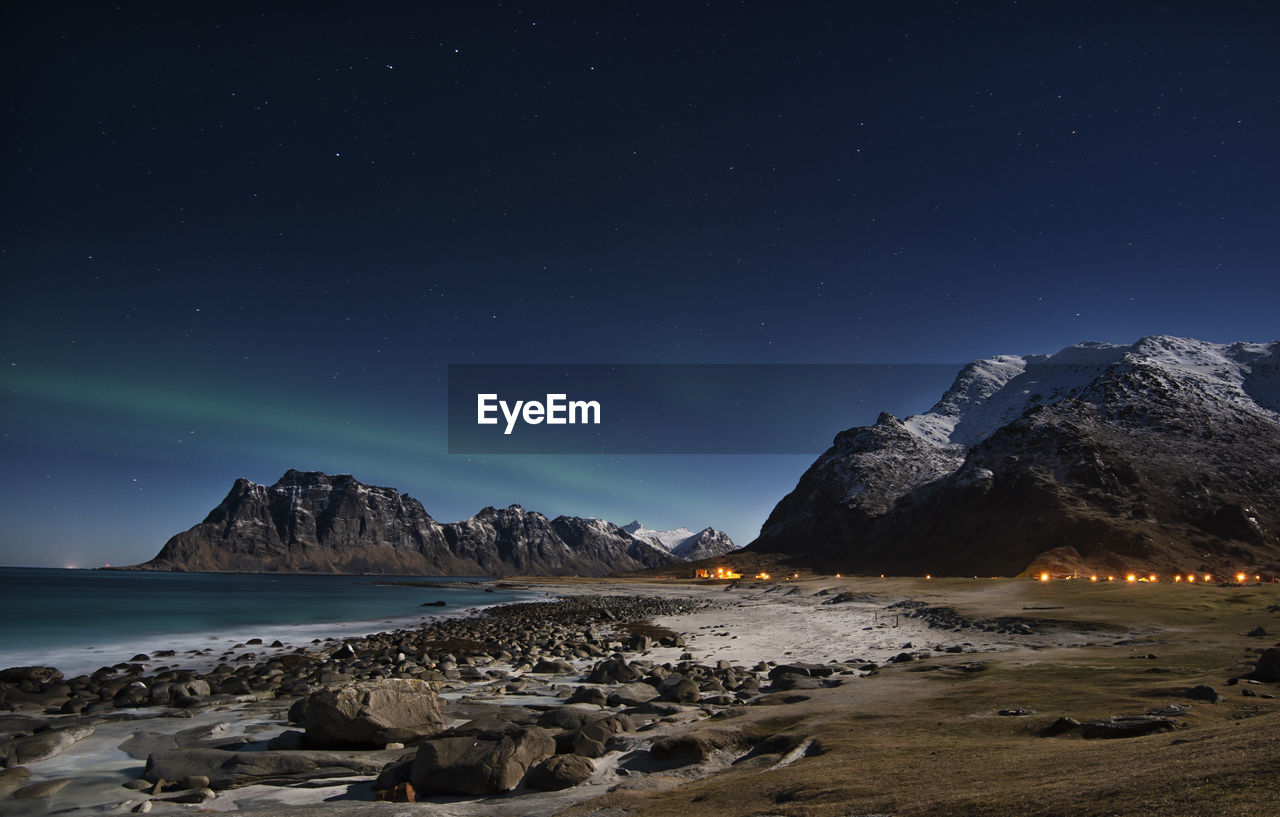Scenic view of sea and mountains against sky at night