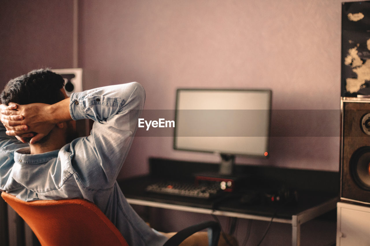 Man relaxing sitting on chair by computer with hands behind head