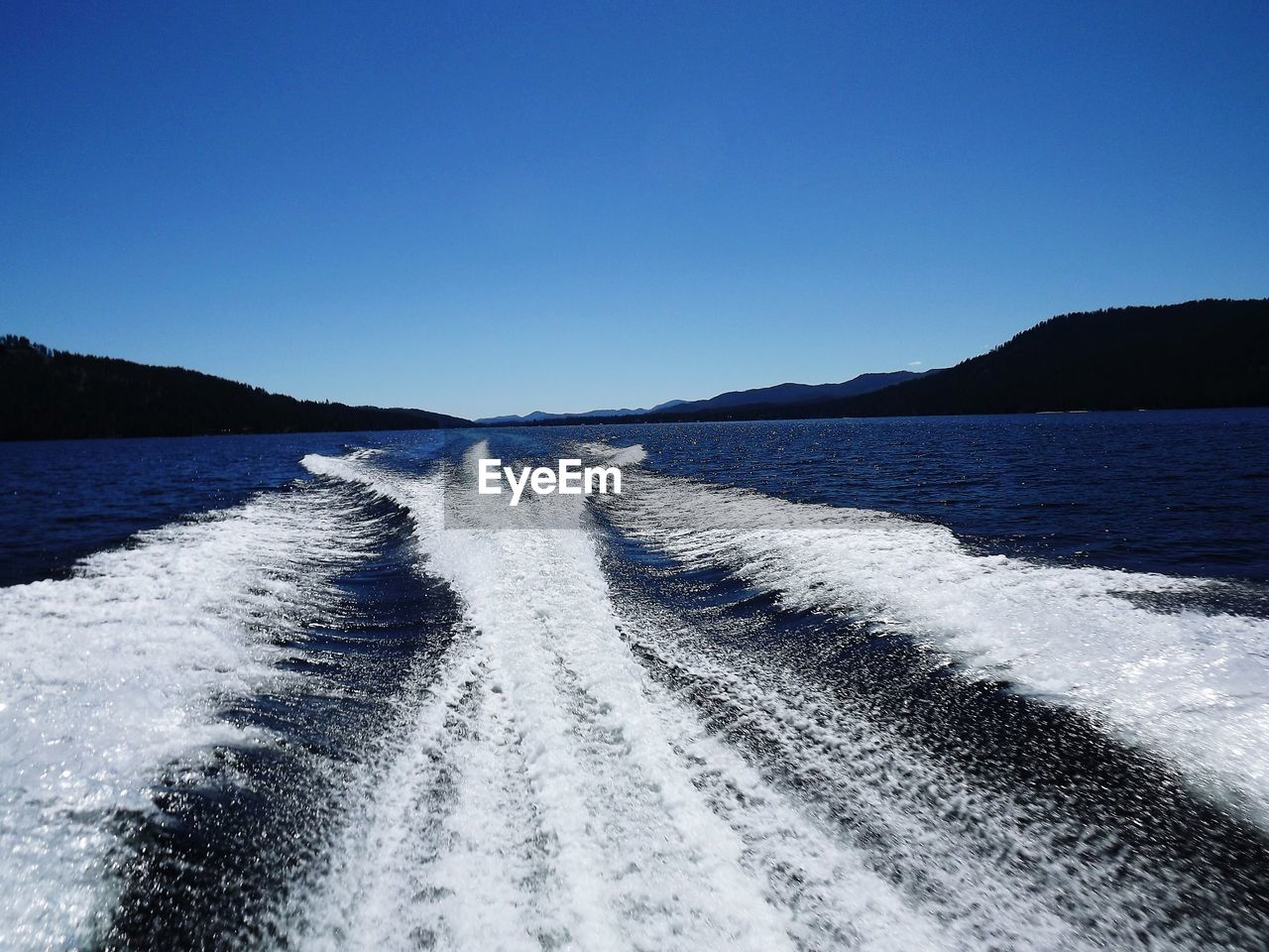 Wake on sea by mountains against clear blue sky