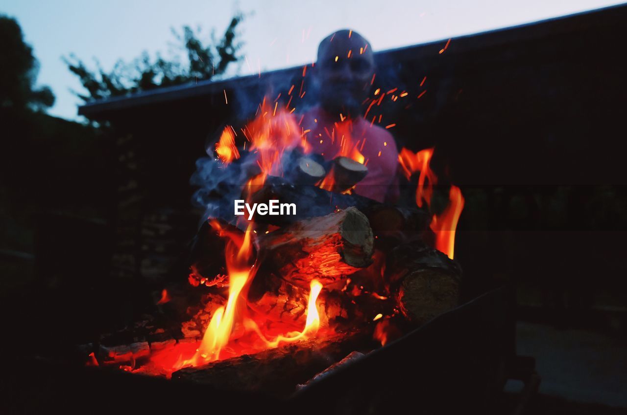 Close-up of burning firewood by man sitting during sunset