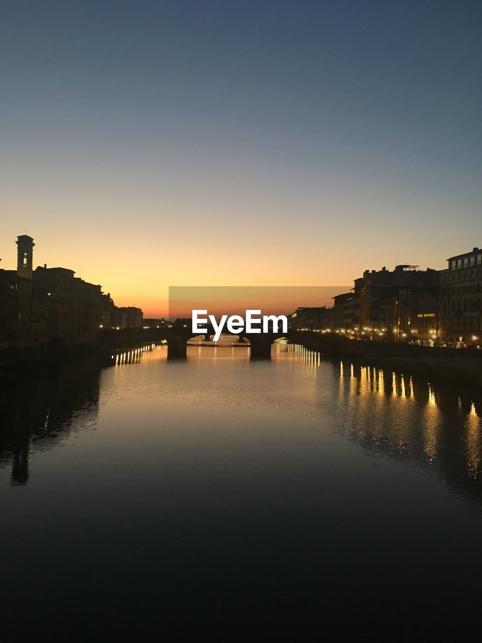 RIVER BY ILLUMINATED BUILDINGS AGAINST SKY AT DUSK